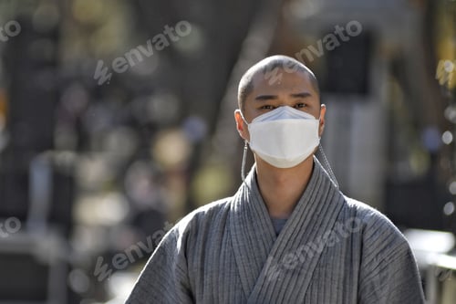 Preview: Portrait of a bald Korean person wearing a facemask and a gray jacket outdoors in South Korea