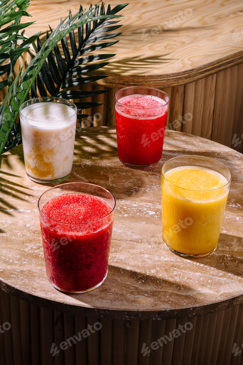 Preview: Four colorful smoothies standing on a wooden table in the sunlight