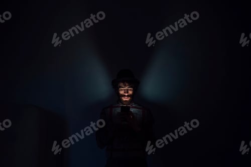 Preview: Bearded young man using smartphone in dark room