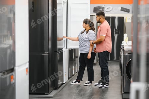 Preview: Young indian couple, satisfied customers choosing fridges in appliances store
