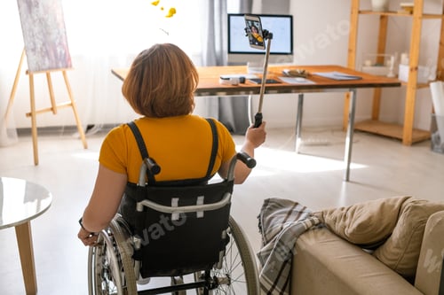 Preview: Back view of young contemporary female in wheelchair moving across her new house