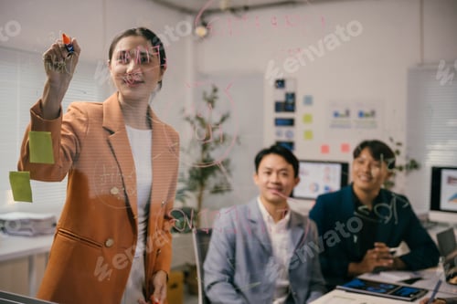 Preview: Asian businesswoman is drawing a business plan on a transparent board during a meeting with her coll