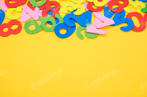Preview: Closeup shot of the colorful wooden numbers scattered on a yellow surface - space for text