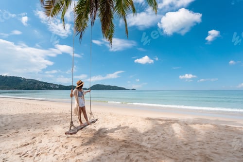 Preview: Young woman traveler enjoying on the swing at beautiful tropical beach