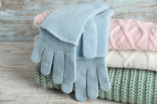 Preview: Stacked sweaters and gloves on wooden table, closeup. Autumn clothes