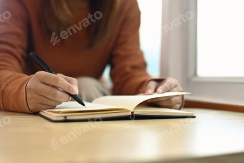 Preview: Unrecognizable young woman writing down future plans and goals in her diary
