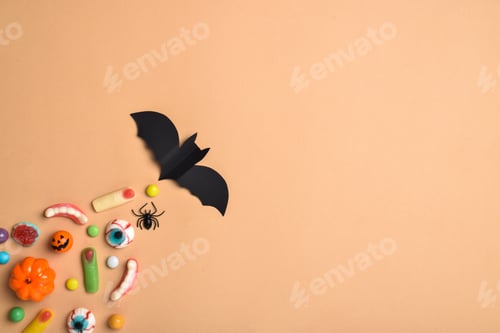 Preview: A bat flies and behind it various sweets on an orange background with a place for text.