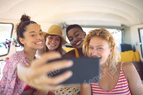 Preview: Happy group of diverse female friends taking selfie with mobile phone in a camper van at beach