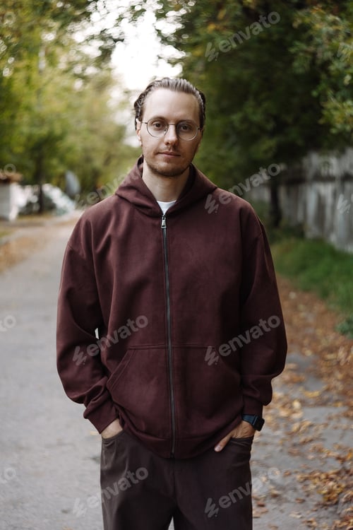 Preview: Young man in brown hoodie standing on park path