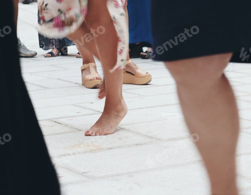 Preview: Young woman dancing barefoot on city street among crowd of people, celebrating life