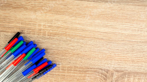 Preview: Pile of a lot multi colored plastic ballpoint pens on wooden table. Abstract stationery background.