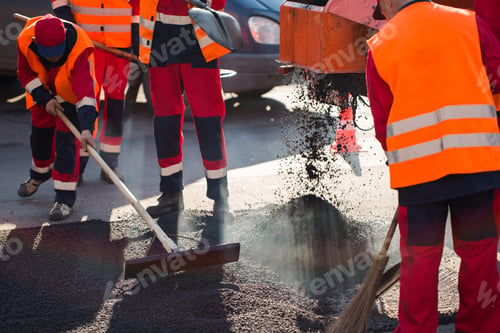 Preview: Worker leveling fresh asphalt on a road construction site, industrial buildings and teamwork