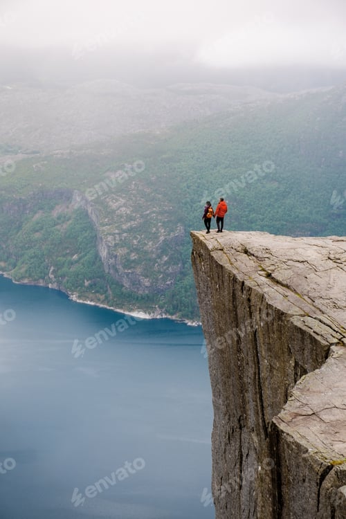 Preview: Two individuals stand on the edge of Preikestolen, a dramatic cliff in Norway, gazing out at the