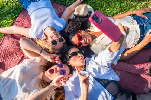Preview: Four playful women taking a selfie lying on blanket in park