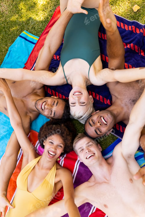 Preview: Portrait of happy diverse group of friends lying on towels and smiling in garden