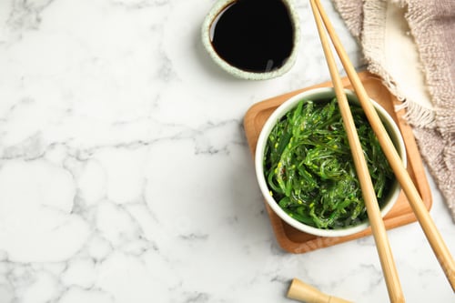 Preview: Japanese seaweed salad served on white marble table, flat lay. Space for text