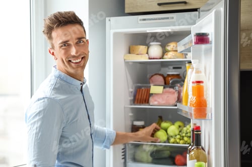 Preview: Man taking apple out of refrigerator in kitchen