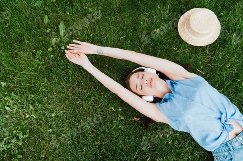 Preview: top view of attractive woman lying on grass and listening music near straw hat