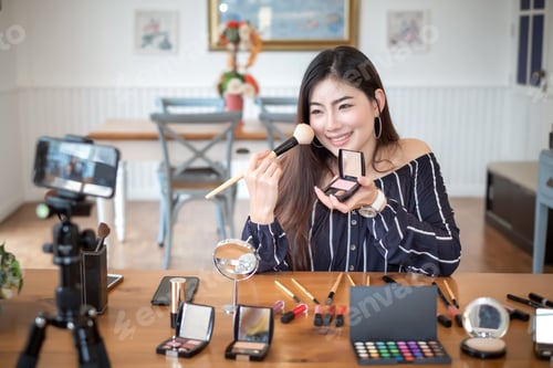 Preview: Asian woman blogger with makeup cosmetics recording video clip by smartphone at home.