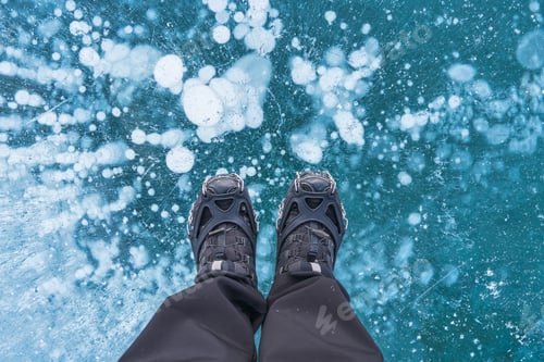 Preview: Man in boots standing on frozen lake with natural bubble in winter