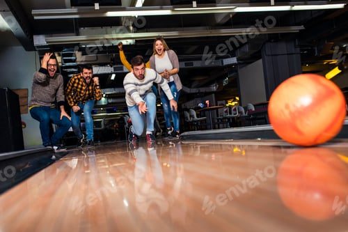 Preview: Group of friends enjoying time together laughing and cheering while bowling at club.