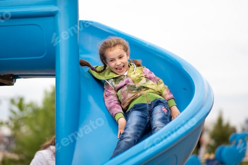 Preview: A little girl on the playground. She on the slide and has a fun.