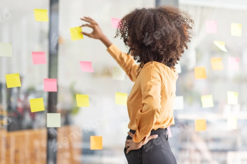 Preview: Young Asian woman Creative team use post it notes to share idea sticky note on glass wall. african b