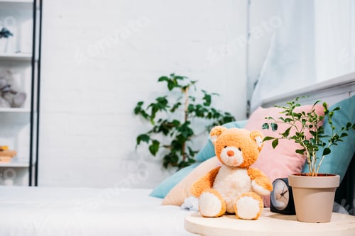Preview: teddy bear with plant and alarm clock in front of bed