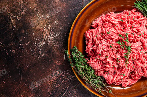 Preview: Raw ground beef or veal meat on a rustic plate with herbs. Dark background. Top view. Copy space