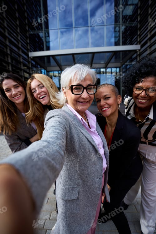 Preview: Group diverse business formal women taking selfie with phone looking smiling at camera.