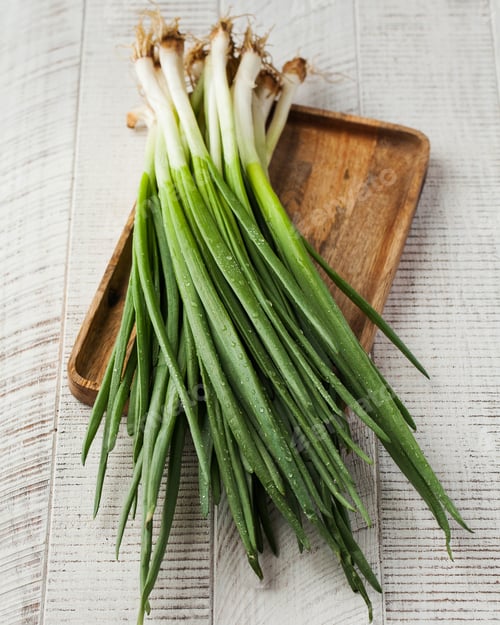 Visualização: Fresh green onions on a wooden board on a light background.