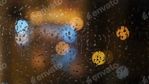 Preview: Close-up of the blurred light spots through the window and raindrops falling down on the glass at