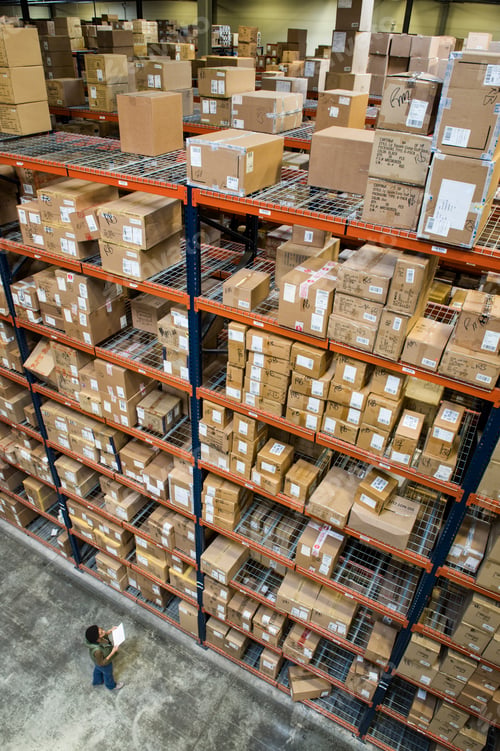 Preview: Warehouse worker checking inventory of boxes on racks in a distribution warehouse.