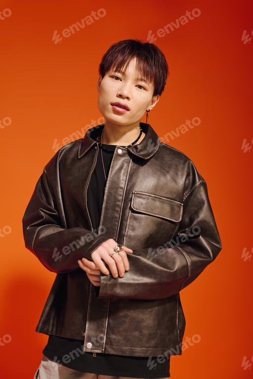 Preview: Stylish young man showcases modern fashion against a vibrant orange backdrop