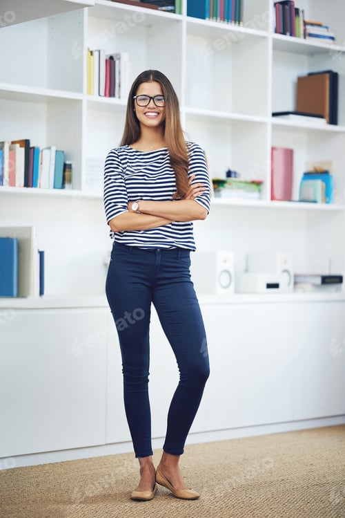 Preview: Portrait of a smiling young woman wearing glasses standing in front of bookshelves at home