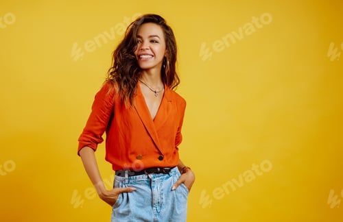 Preview: Portrait of young girl posing on yellow background. Pretty woman wears a carrot blouse and jeans.