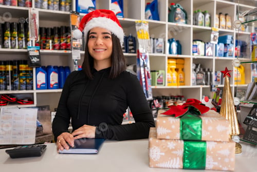 Preview: Smiling woman wearing a santa hat and black hoodie working at an auto parts store register