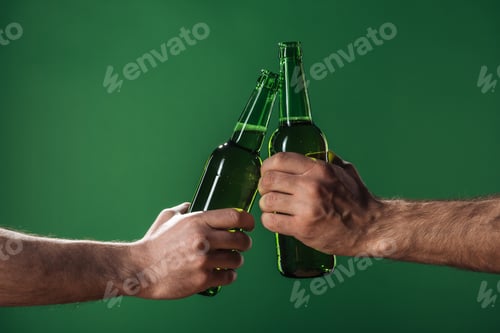 Preview: cropped view of men clinking beer bottles isolated on green, st patrick day concept