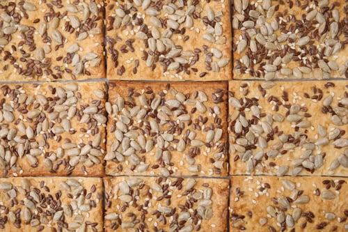 Preview: Cereal crackers with flax, sunflower and sesame seeds as background, top view