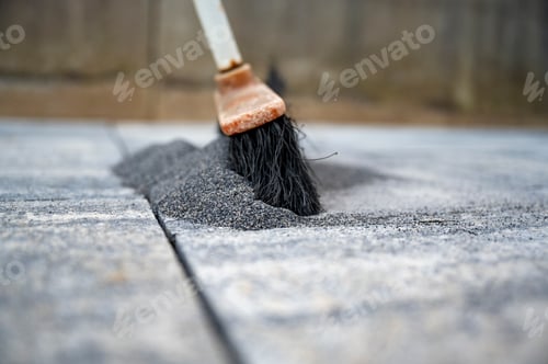 Preview: Broom pushing a tile gaps sand in between concrete tiles for outdoor patio