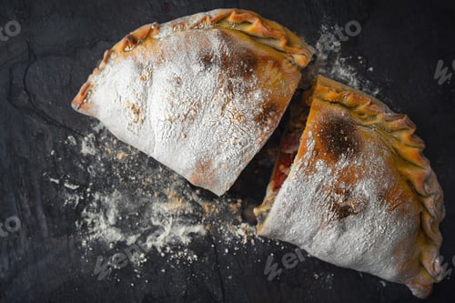 Preview: Sliced calzone with flour on the dark stone background top view