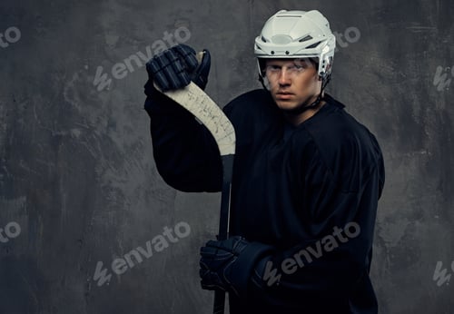 Preview: Hockey player wearing black protective uniform holds a hockey stick on a gray background.