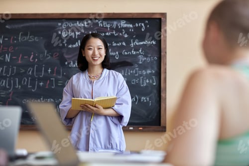 Preview: Young successful female student with open book looking at classmate