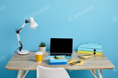 Preview: workplace with laptop and lunch box on wooden table on blue background, illustrative editorial