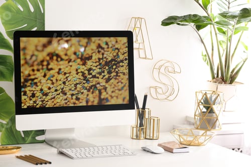 Preview: Modern workplace with computer and golden decor on desk near wall. Stylish interior design