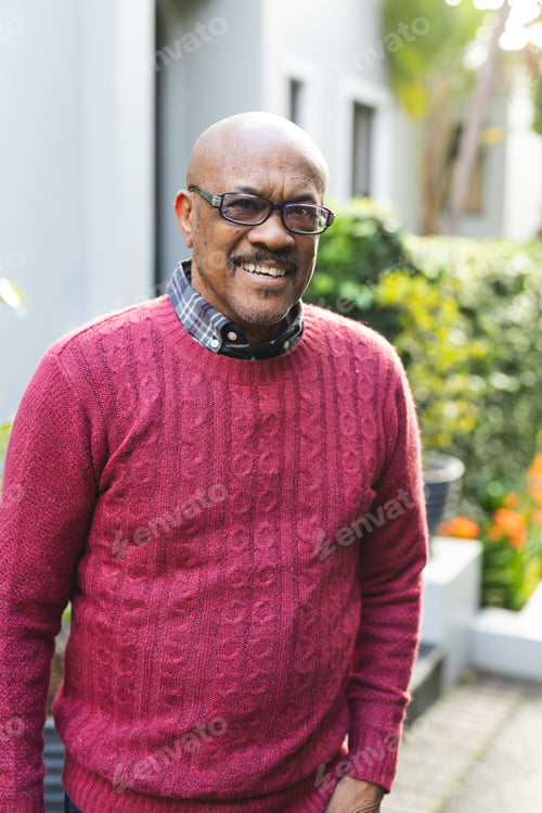 Preview: Portrait of happy senior african american man wearing glasses and red jumper standing outside house