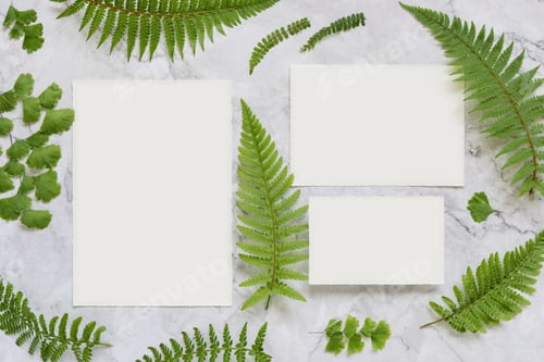 Preview: Wedding paper cards and envelope on marble table with fern leaves top view