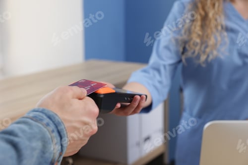 Preview: Receptionist taking payment from patient via terminal in clinic, closeup