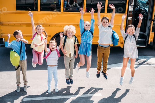 Preview: group of adorable schoolchildren jumping in front of school bus and looking at camera