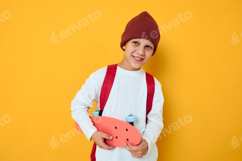 Preview: happy schoolboy in a red hat skateboard in his hands yellow color background